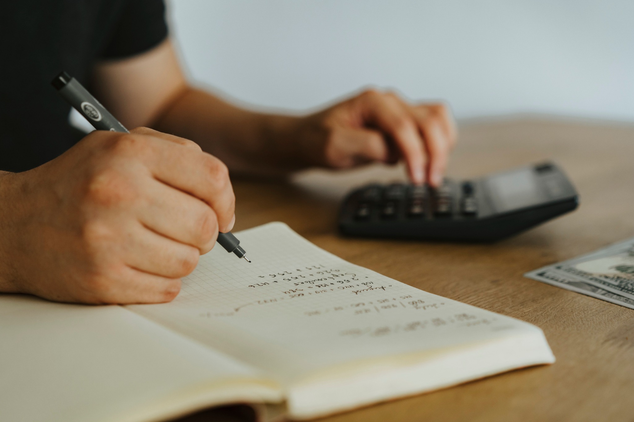 Person writing a financial plan beside a calculator and cash