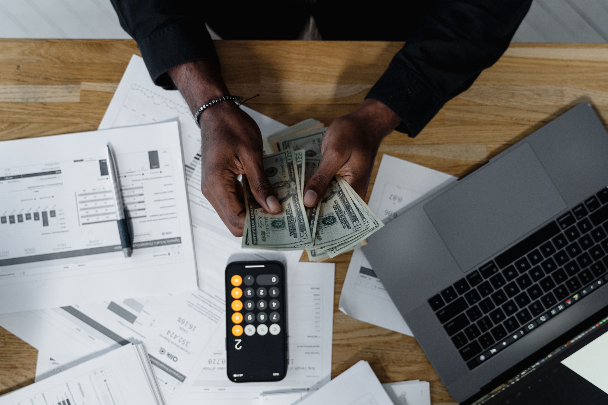 Person counting cash beside a laptop, calculator and financial paperwork