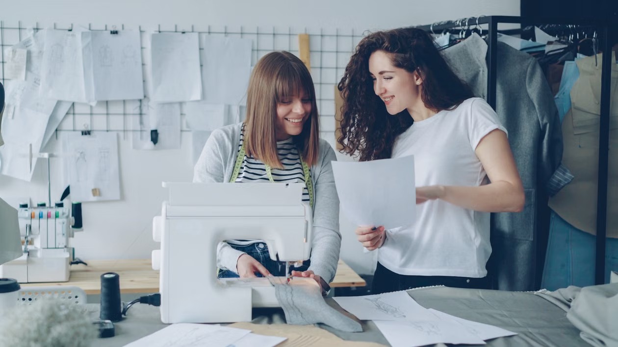 Two small-business makers reviewing a design beside a sewing machine