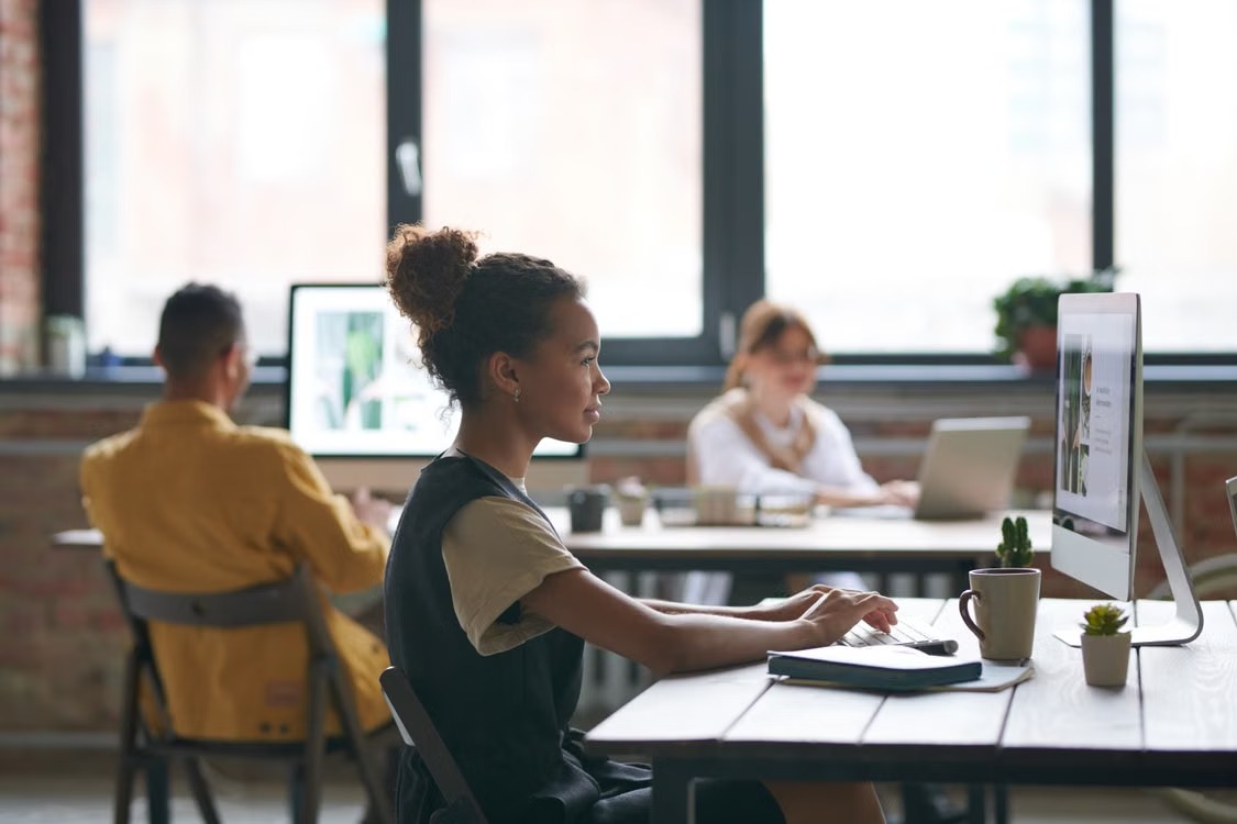A small creative team member working at a desktop computer in a shared workspace
