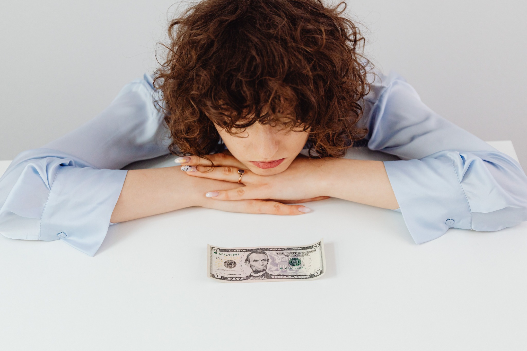 A woman resting her head on her arms with a five-dollar bill in front of her