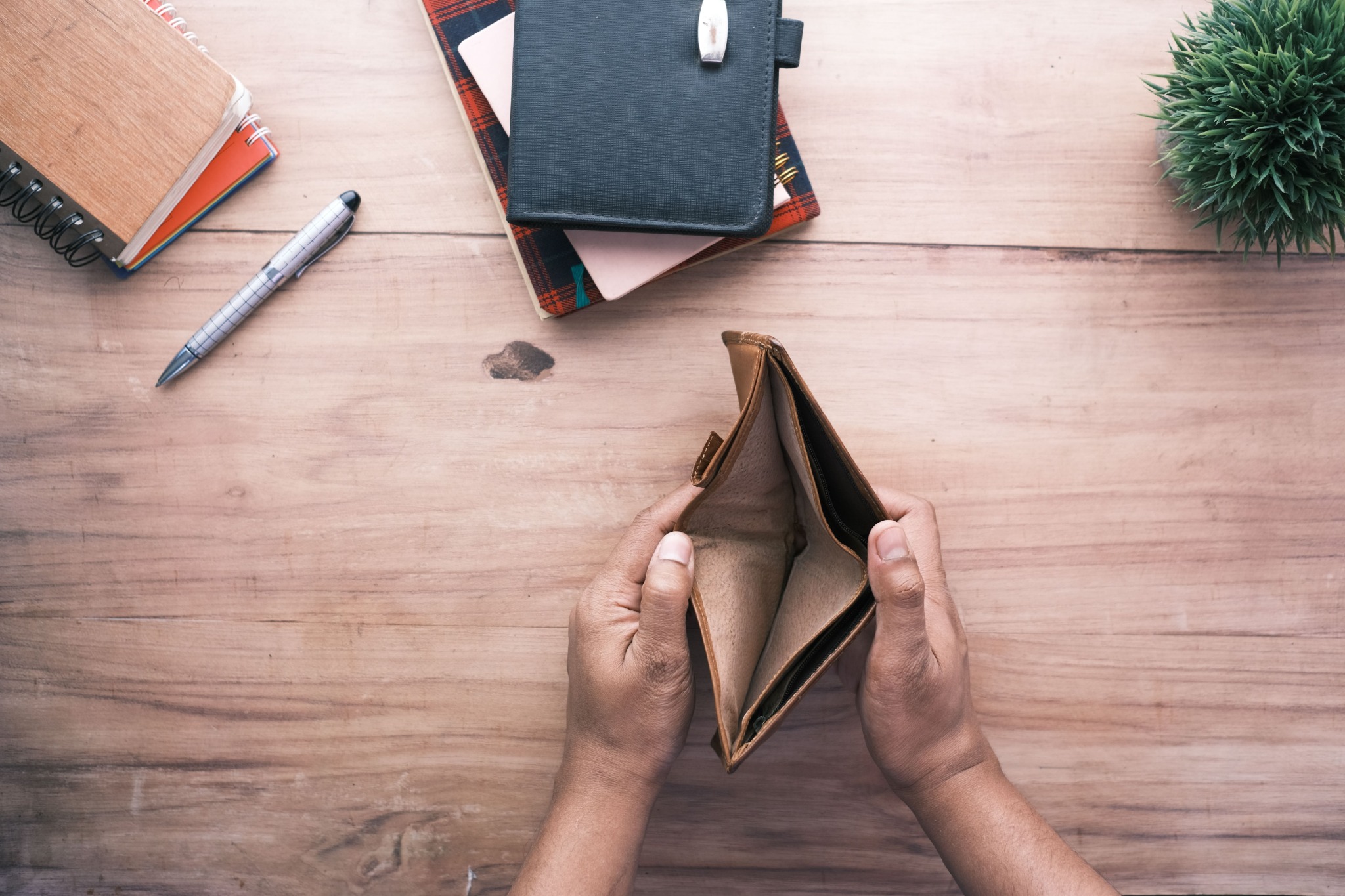 Hands holding an open empty wallet on a wooden desk